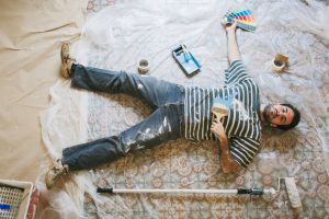 One young man is lying down on the floor after a hard days work painting his new apartment.