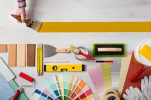 Decorator holding a paint brush and painting a wooden surface, work tools and swatches at bottom, banner with copy space
